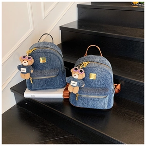 Dettaglio di due zaini in denim con zip dorate e graziosi ciondoli a forma di orsetto