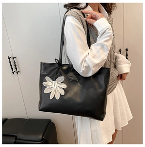 Side view of a large black tote bag on model, featuring a white floral pendant and logo tag