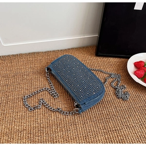 Detail of blue denim crossbody bag featuring silver stud embellishments and a metal chain