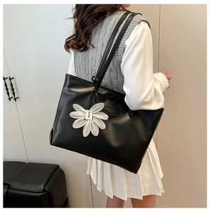 Detail of black matte leather tote bag featuring a white 3D daisy charm for daily commute