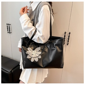 Detail of a black large tote bag featuring a white flower charm and long shoulder straps