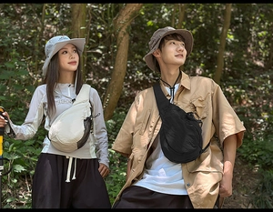 Outdoor crossbody bag in beige and black colors with side mesh pockets in nature setting