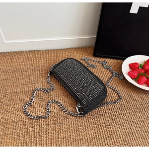 Detail shot of black rhinestone shoulder bag with silver metal chain on a woven mat
