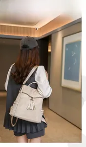 Detail of beige PU leather backpack featuring tassel charms and metal zipper pocket
