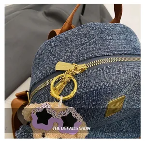Dettaglio dello zaino in denim con hardware dorato e portachiavi orsetto viola