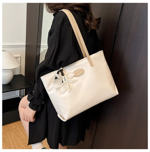 Close-up of a white tote bag with brown handles and a 3D white floral charm detail