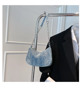Detail view of light blue denim half-moon underarm bag hanging on a silver metal stand