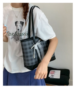 Detail of checkered tote bag featuring lace bow and pearl charm with black leather handle