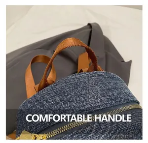 Dettaglio dello zaino in denim blu con manico in nylon marrone e cerniera in metallo dorato