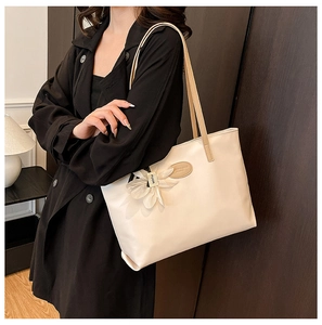 Close-up of cream white leather tote bag with elegant flower charm and metal logo detail