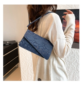 Detail of dark blue snakeskin texture handbag worn with a cream knit sweater