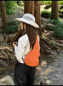 Detail of vibrant orange nylon chest bag featuring side mesh pocket in an outdoor setting