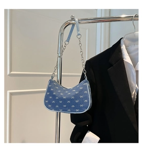 Detail of blue denim hobo bag featuring white bow prints and silver chain strap