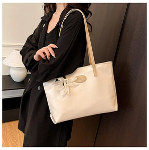 Detail of cream tote bag featuring a white floral charm and smooth faux leather texture