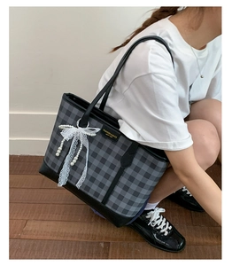 Detail of grey plaid tote bag with white lace bow, pearl charm and leather straps