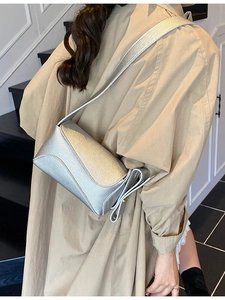 Silver lychee pattern crossbody bag with adjustable strap worn by model in trench coat