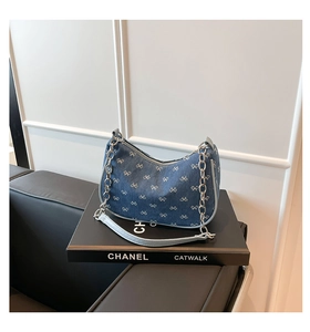Detailed macro of denim hobo bag featuring white bow patterns and silver chain strap