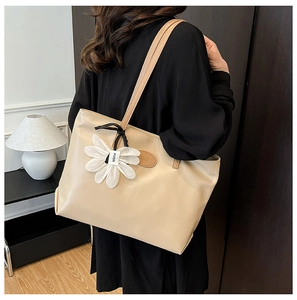 Detailed back view of a large beige tote bag with floral charm and logo patch on model