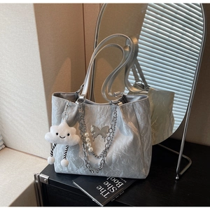 Detail of silver crinkled tote bag with butterfly charm, pearl chain and cloud plush toy