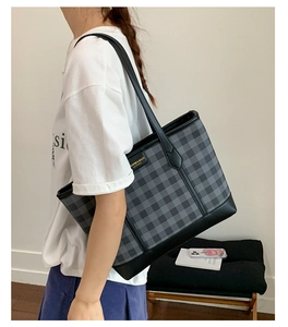 Close-up of black and grey checkered tote bag with leather straps and gold metal logo plate