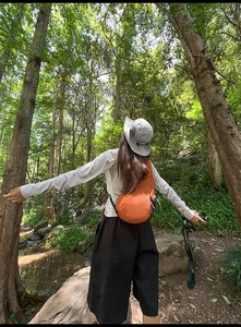 Detail of an orange Oxford fabric crossbody bag shown in a forest hiking scenario