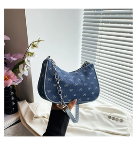 Close-up of blue denim crescent bag featuring white bow embroidery and silver metal chain