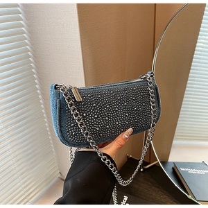 Detail of blue denim baguette bag featuring silver studs and metallic chain strap
