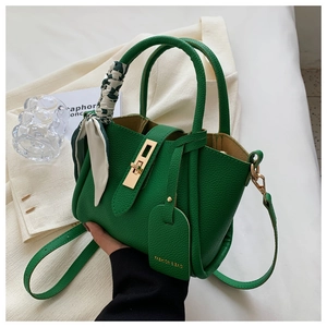 Détail du sac seau en cuir vert vif avec fermoir doré et poignée ornée d'un foulard en soie