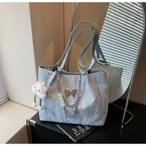 Detail of light blue pleated tote bag with silver butterfly charm and pearl chain