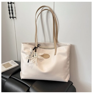Close-up of cream leather tote bag featuring a floral charm and contrast brown strap