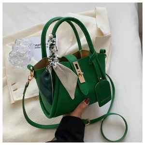 Gros plan d'un sac seau vert texturé avec un fermoir doré et un foulard en soie élégant