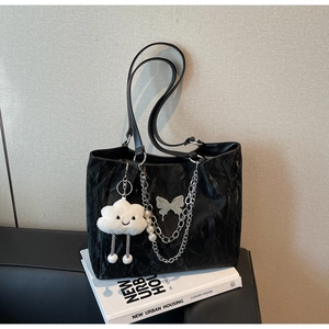 Detail of black tote bag featuring silver butterfly charm, chains and a cloud pendant