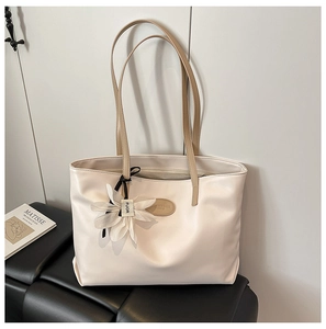 Detailed shot of a beige tote bag featuring a leather floral charm and metal fashion plate