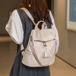 Close-up of beige textured leather backpack featuring double tassel charms and metal zipper