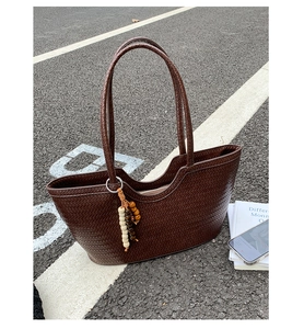 Detail of dark brown woven leather tote with vintage wooden bead tassel on asphalt background