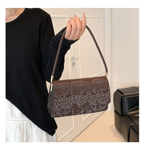 Close-up of brown snake-embossed leather texture with metallic gold hardware on handbag