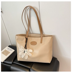 Detail of beige tote bag with brown straps and white flower charm on a black bench
