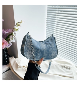 Detail view of denim blue crescent underarm bag with silver chain and white washed texture