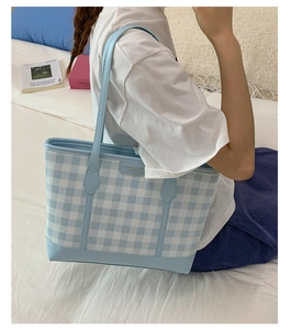 Close-up of a blue gingham tote bag with golden lettering shown on a shoulder
