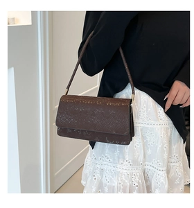 Detail of dark brown faux snakeskin shoulder bag with gold hardware on a female model