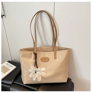 Detail view of beige tote bag with daisy charm on a leather bench in minimalist setting