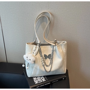 Detail of cream white tote bag featuring metallic chain, pearls and a butterfly logo