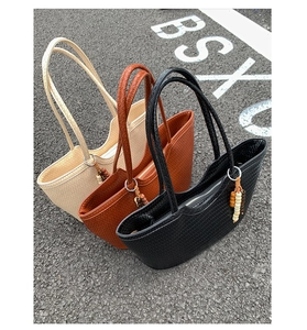 Detailed view of woven tote bags in beige, tan, and black with beaded tassel charm