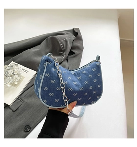 Detail of dark blue denim crescent bag featuring white bow patterns and silver chain
