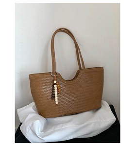 Close-up of brown woven tote bag featuring diamond pattern and ethnic wood bead pendant