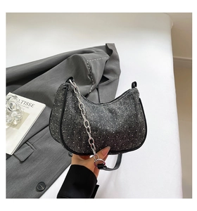Detail of dark grey crescent denim bag with white polka dots and silver chain strap