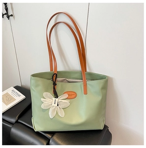 Detailed close-up of large light green tote bag with brown straps and white flower charm