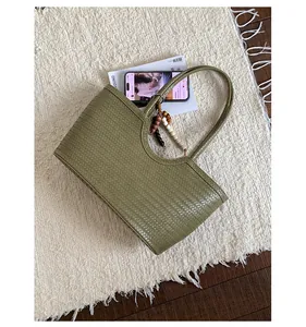 Detail of olive green woven tote bag with wooden bead charm on a soft white texture