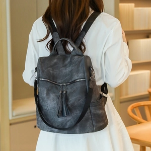 Detail of dark gray vintage backpack featuring a metal zipper and long tassel accents
