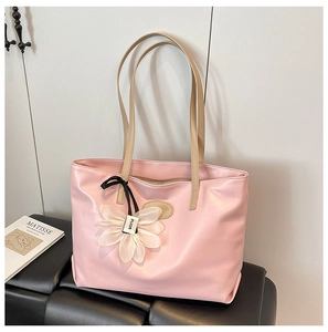 Detail shot of pink tote bag featuring a floral charm and sleek brown leather shoulder strap
